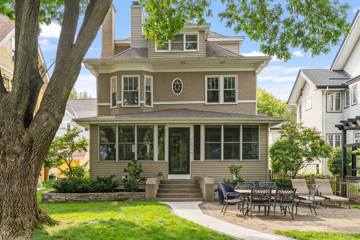 Classic two-story home with inviting front porch and private patio dining area, nestled in a tree-lined residential neighborhood.