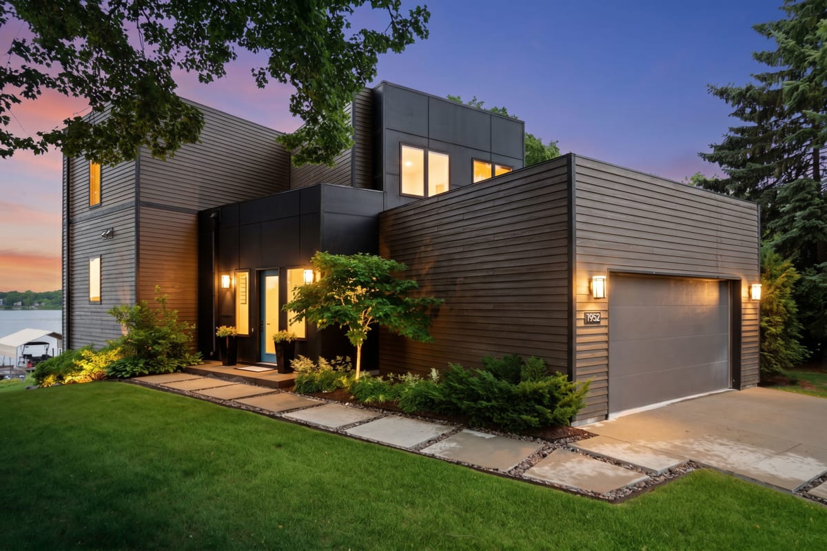 Modern lakeside retreat with sleek architecture, welcoming entrance lighting, and beautifully landscaped grounds, set against a stunning twilight sky with lake access nearby.
