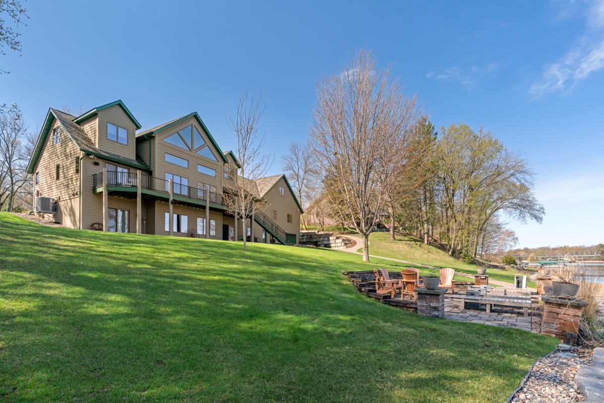 Spacious lakeside retreat featuring multiple levels, outdoor fire pit, and expansive lawn sloping toward the water.