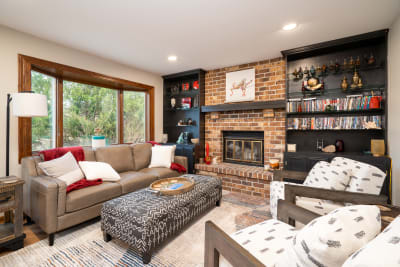 A comfortable living room with a beige leather sofa, patterned ottoman, and black shelving unit.