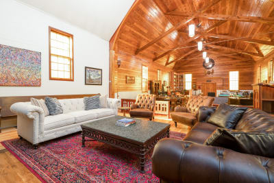 A spacious living room featuring a white Chesterfield sofa, dark leather couch, a decorative coffee table, and vibrant artwork on the walls.