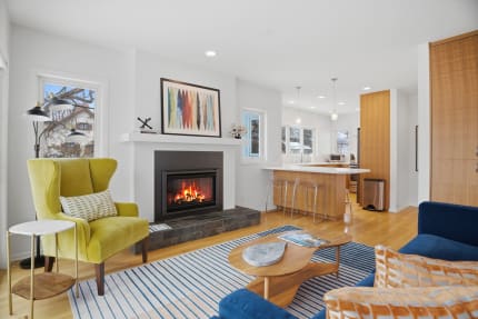 A modern living room with a cozy fireplace, green accent chair, and stylish furniture, illuminated by natural light.