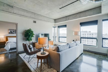 Contemporary living room featuring a gray sofa, geometric armchair, and panoramic city view through large windows.