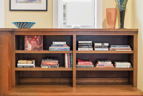 A warm wooden bookshelf filled with varied books and decorative items, illuminated by natural light from a window.
