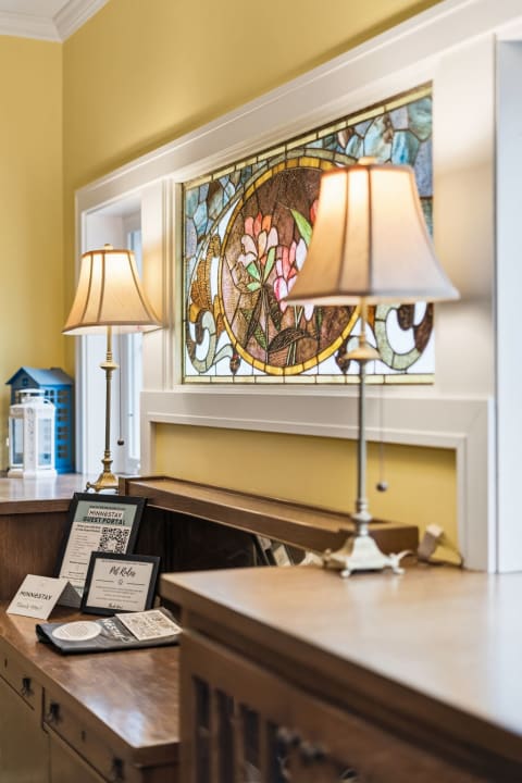 Stained glass window featuring floral design and warm interior decor with lamps and documents on a wooden surface.