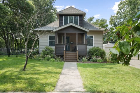 A two-story house with a wooden porch, surrounded by a well-maintained lawn and plants.