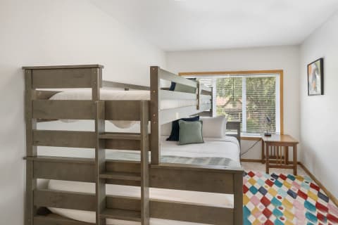 A serene bedroom featuring a gray wooden bunk bed and a colorful geometric rug on the floor.