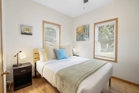 A well-lit bedroom with a bed, nightstand, and artwork on the walls.