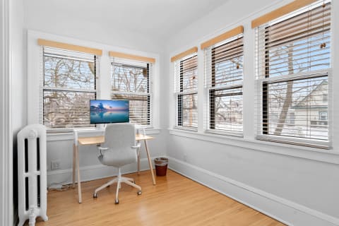Cozy office space with a desk, chair, and large windows showing trees outside.