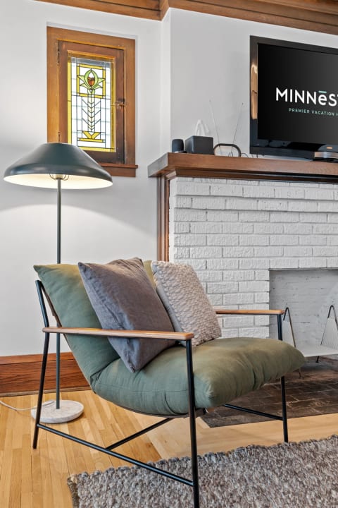Cozy living room setup with a green chair, pillows, floor lamp, and stained glass window.