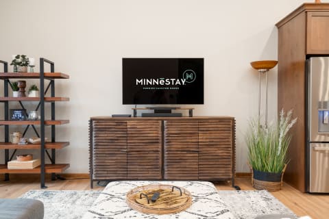 Modern living room with a TV, wooden console, and decorative items on shelves.