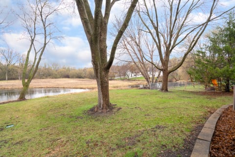 A serene pond scene with trees and a house in the background.