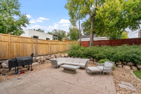 Cozy backyard patio with modern seating and grill, set against a lush green backdrop.