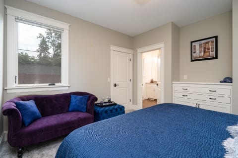Cozy bedroom featuring a blue bedspread, purple loveseat, and a modern aesthetic.