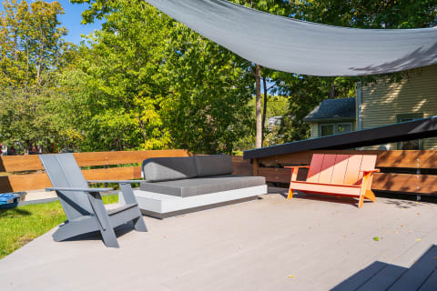 Stylish outdoor seating with grey and orange chairs, a grey sofa, and a fabric canopy amongst greenery.