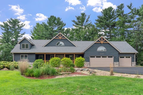 A charming blue house with a porch and two-car garage, surrounded by trees and landscaped gardens.
