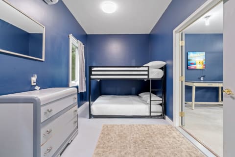 A cozy room featuring a bunk bed, dresser, and modern desk with a TV.