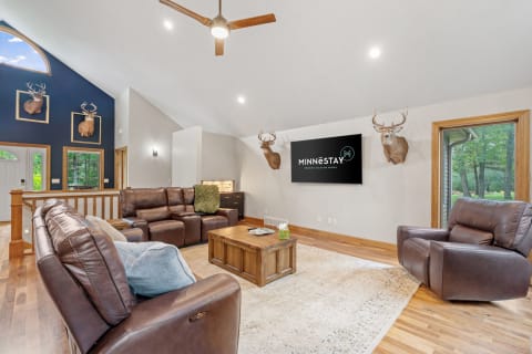 Spacious living room featuring leather sofas, rustic decor, and a large window with views of nature.