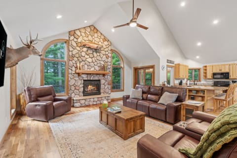 Cozy living room with stone fireplace and leather sofas, overlooking greenery.
