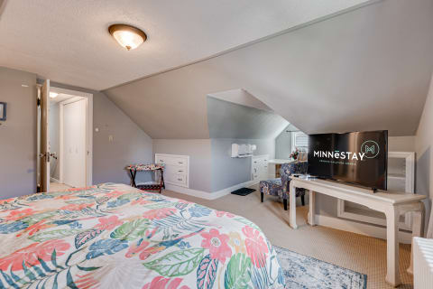 A cozy attic bedroom with floral bedding, sloped ceilings, and a television.