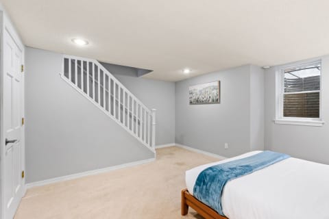 Basement bedroom with gray walls, beige carpet, and a bed with aqua throw blanket.