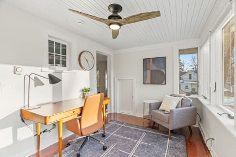 A cozy workspace featuring a wooden desk, a stylish chair, and large windows with natural light.