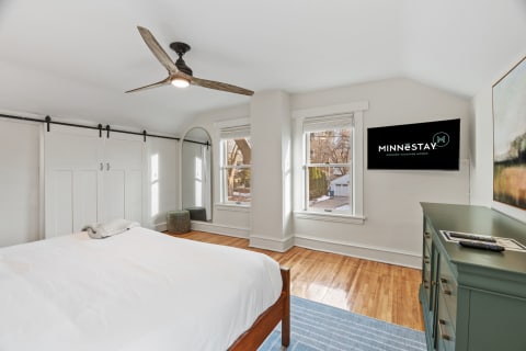 Bright and serene bedroom with a large bed, sliding barn doors, and a television mounted on the wall.