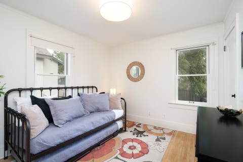 A modern bedroom with a metal daybed, decorative pillows, and a floral rug.