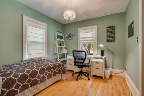 A modern bedroom with green walls, a single bed, a workspace, and motivational wall art.