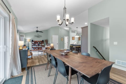 A spacious dining room with a wooden table, black chairs, and stylish living area in the background.