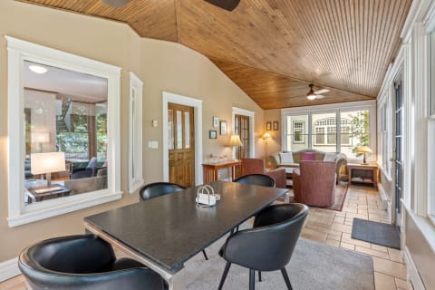 Interior view of a cozy dining and living area with wooden ceiling and large windows.