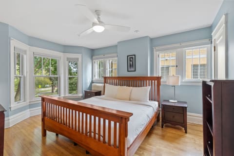 Cozy bedroom with wooden furniture, blue walls, and large windows.