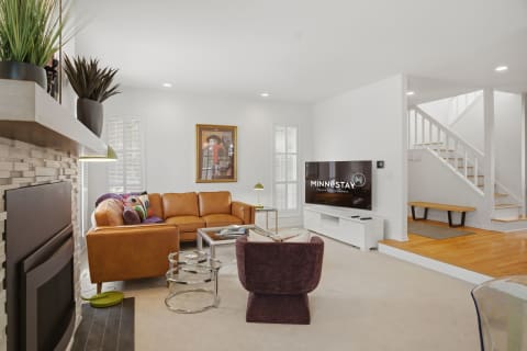 Modern living space featuring a leather sectional sofa, glass coffee table, and a large television, with a staircase in the background.