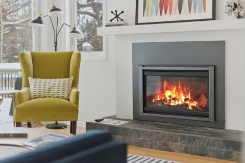 Cozy interior with a mustard wingback chair and a modern fireplace, framed by snowy windows.