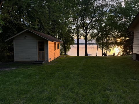 A lakeside cabin at sunset with lush greenery and calm waters.