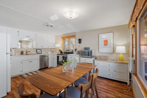 A stylish kitchen with white cabinets, marble countertop, and a wooden dining table with plants.