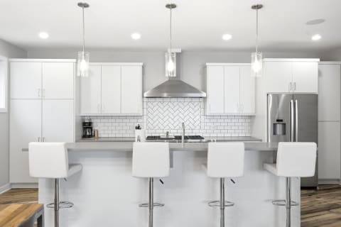 A bright, modern kitchen featuring white cabinetry, a herringbone tile backsplash, and stainless steel appliances.