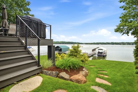 A view of a waterfront property featuring steps leading down to a lake, a boat dock, and lush landscaping.