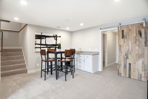 Modern basement bar area featuring high-top table, kitchenette, and rustic barn door.