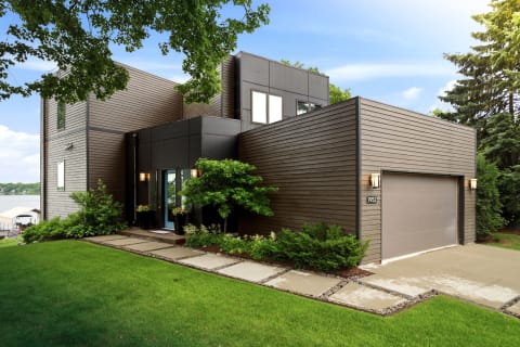 Modern lakeside home with horizontal siding, lush greenery, and a serene background.