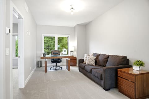 A cozy workspace with a large window, a wooden desk, an office chair, and a comfortable sofa.