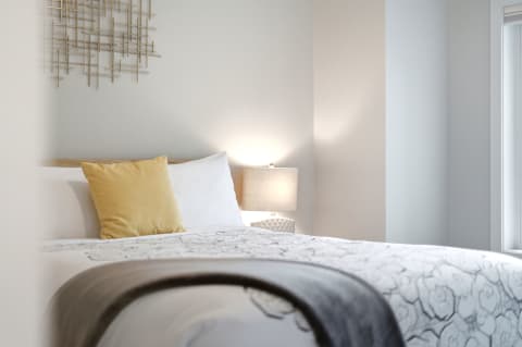 Cozy bedroom with a bed, warm lighting, and modern decor featuring a golden pillow and stylish wall art.