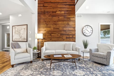 A cozy living room with a wooden accent wall, light grey furniture, and a lakeside view.