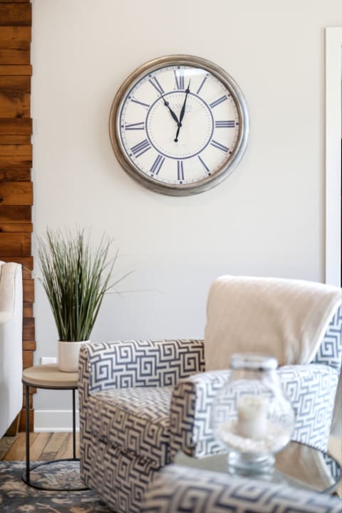 A stylish living room with a large clock, patterned armchair, and decorative plant, creating a cozy atmosphere.