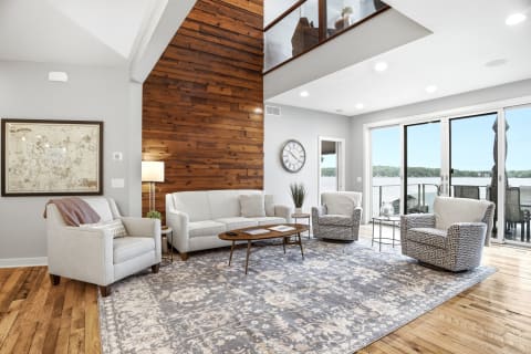 A modern living room with a wooden feature wall, plush seating, and large windows offering waterfront views.