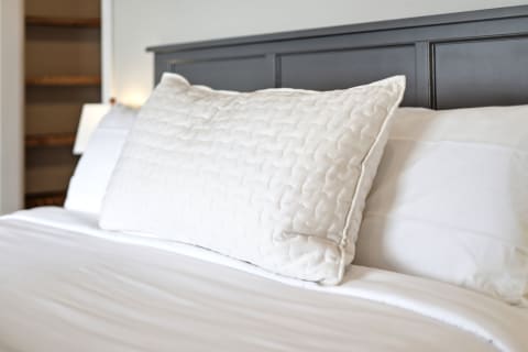 A luxurious bedroom featuring a quilted white pillow on a neatly made bed with crisp linens and a dark wood headboard.