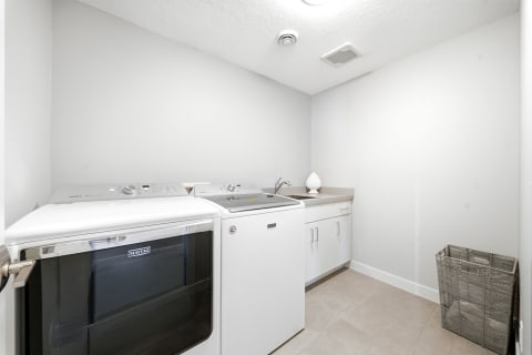 A tidy laundry room featuring a washer, dryer, countertop, sink, and a laundry basket.