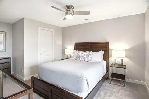 A stylish bedroom featuring a wooden bed frame, plush bedding, nightstands with lamps, and a ceiling fan.