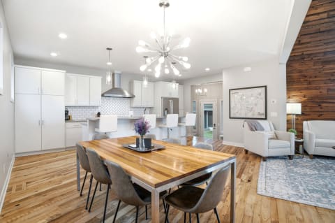 Modern dining area with wooden table and stylish chairs, adjacent to a well-equipped kitchen, illuminated by contemporary lighting fixtures.