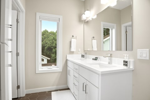Modern bathroom with white cabinetry, dual sinks, and natural light from a window.